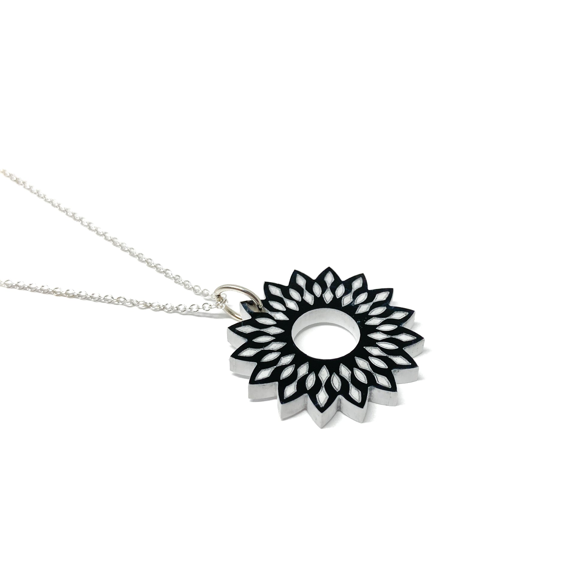 A silver necklace featuring a black and white mandala pendant with a stylized floral and geometric design and a central open circle.