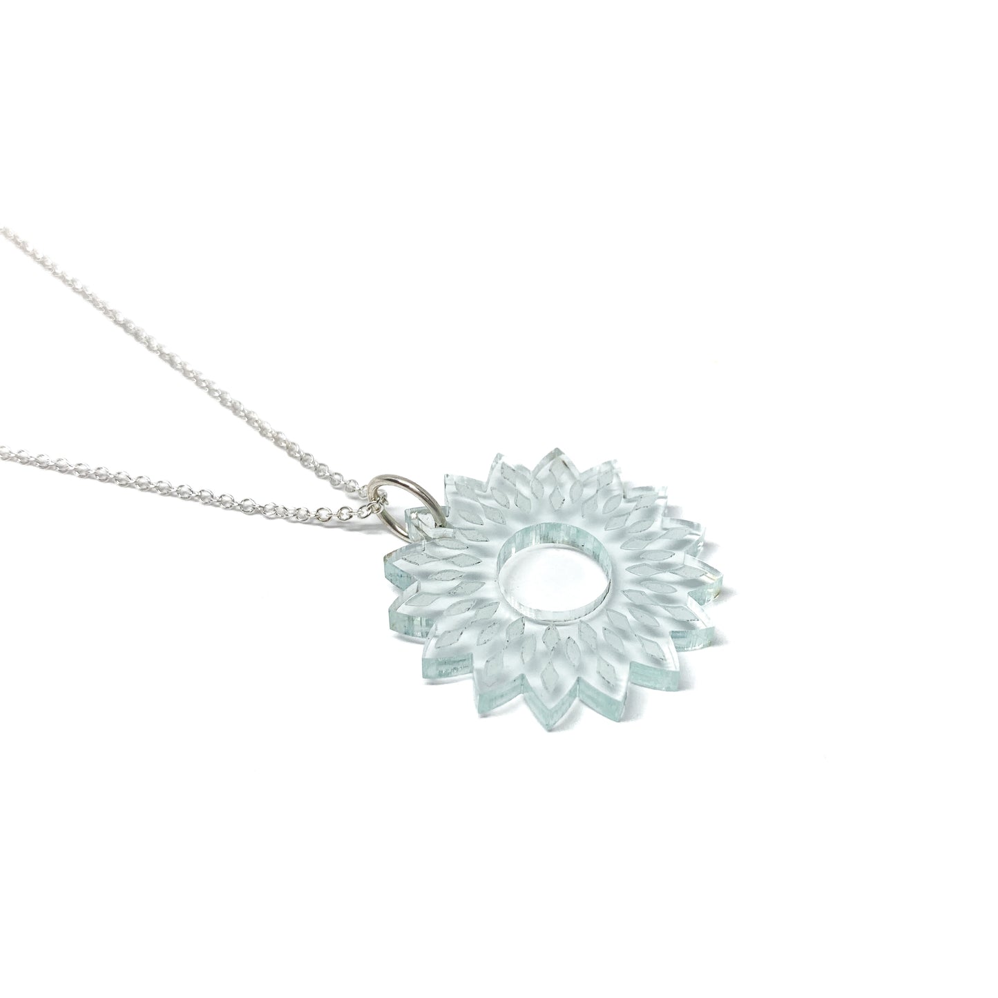 A silver necklace featuring a translucent light blue mandala pendant with a stylized floral and geometric design and a central open circle.