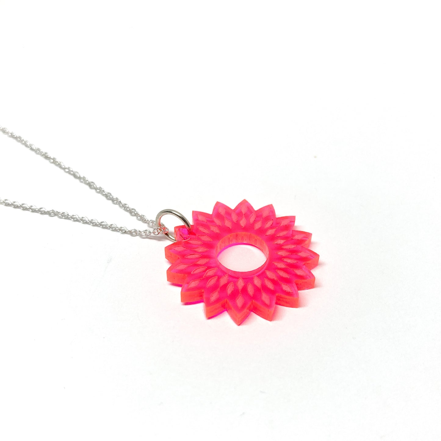 A silver necklace featuring a translucent pink mandala pendant with a stylized floral and geometric design and a central open circle.