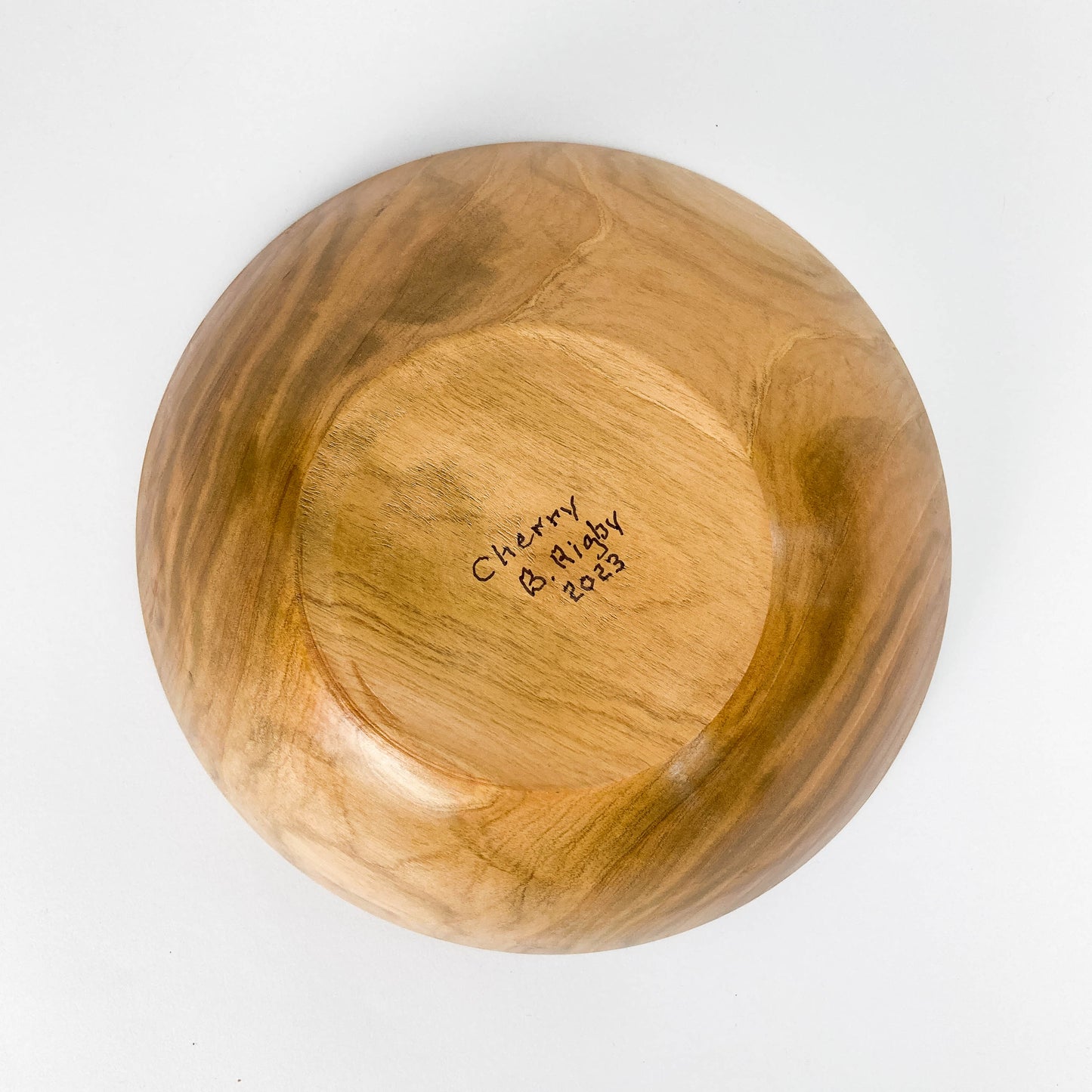 A wooden bowl, viewed from above, showing the artist's name "B. Rigby" and the year "2023" inscribed on the inside.