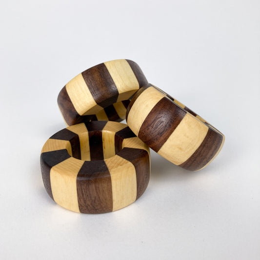Three wood napkin rings with alternating dark and light wood stripes, stacked casually.
