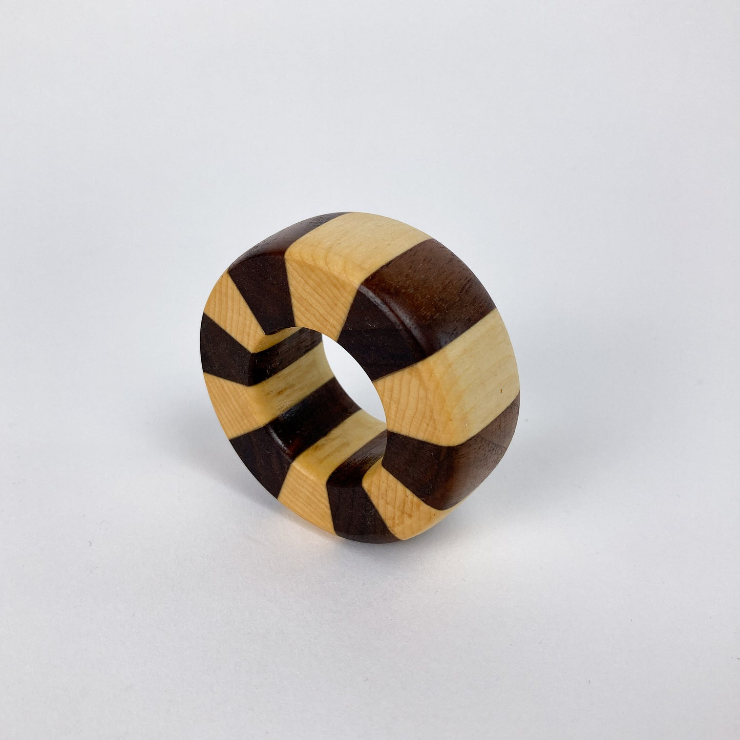 A single wood napkin ring with alternating dark and light wood stripes, presented upright.