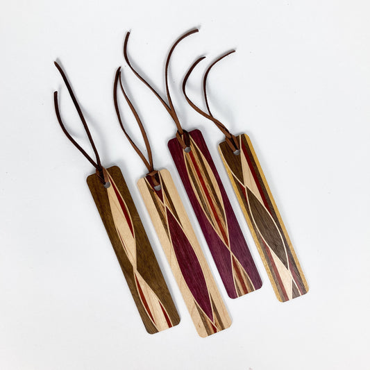Four woven wooden bookmarks with flowing, contrasting wood grain patterns and leather cords.