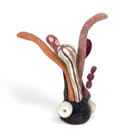 Whimsical felted wool sculpture with various textured and patterned organic forms emerging from a dark base.