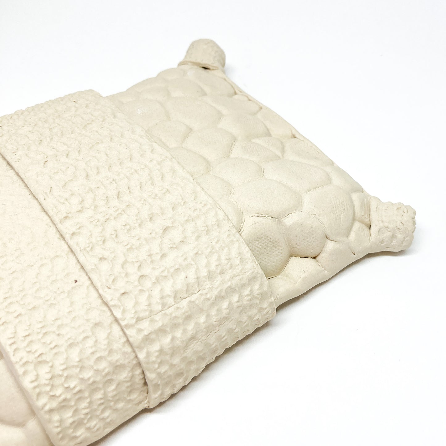 Close-up of a textured, diamond-shaped pillow wall sculpture with a central band and corner cylinders.