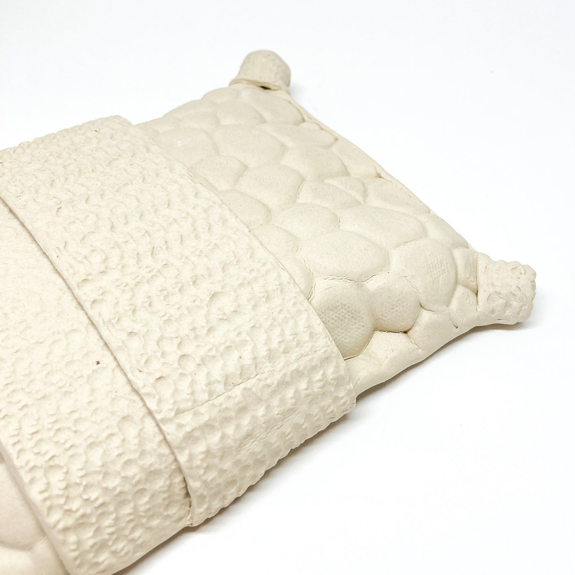 Close-up of a textured, diamond-shaped pillow wall sculpture with a central band and corner cylinders.