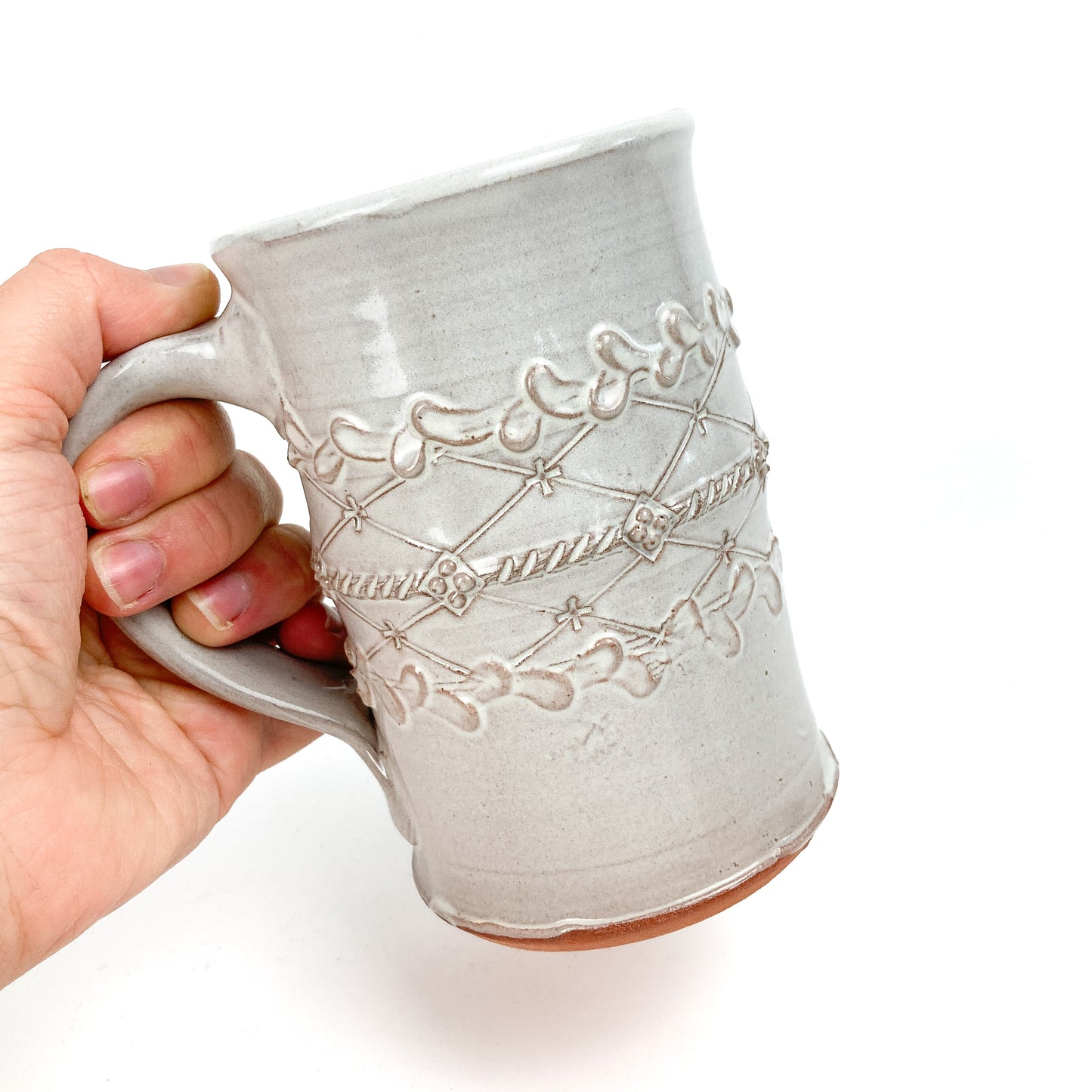 Hand holding a ceramic Coral Patola Trellis Stein with raised coral and garland decoration.