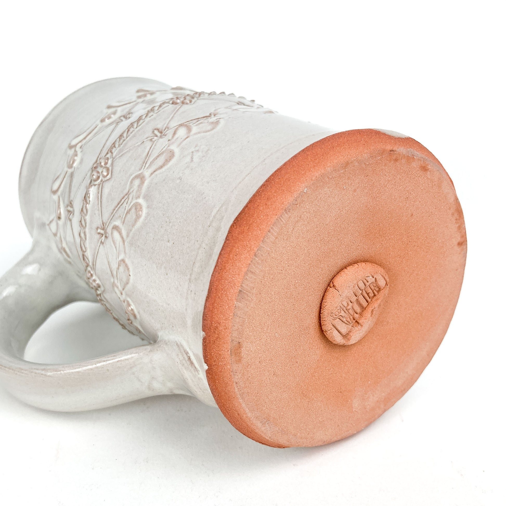 Bottom view of a Coral Patola Trellis Stein showing the unglazed base and "Cotton Pottery" stamp.