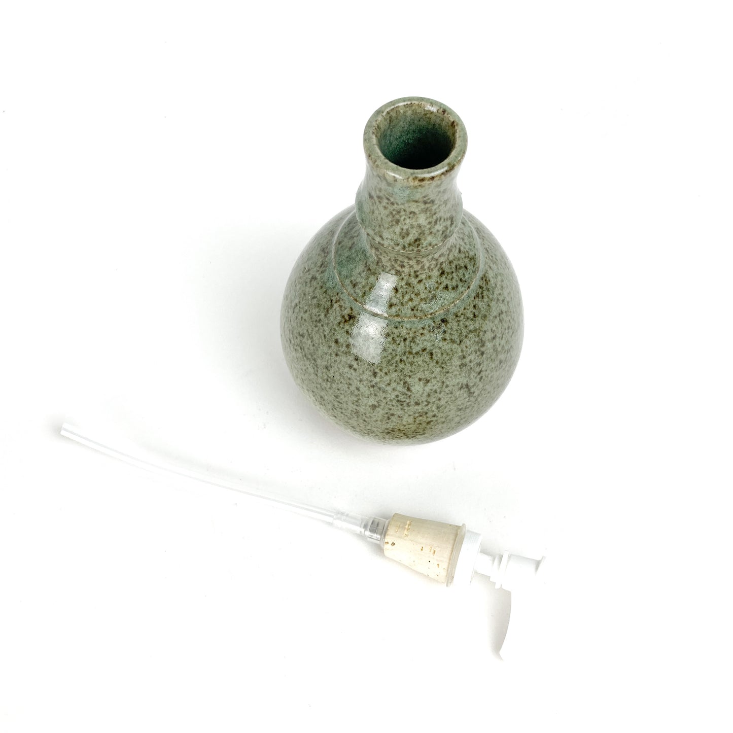 Top-down view of a Coral Patola Celadon pump bottle with the pump mechanism detached beside it.