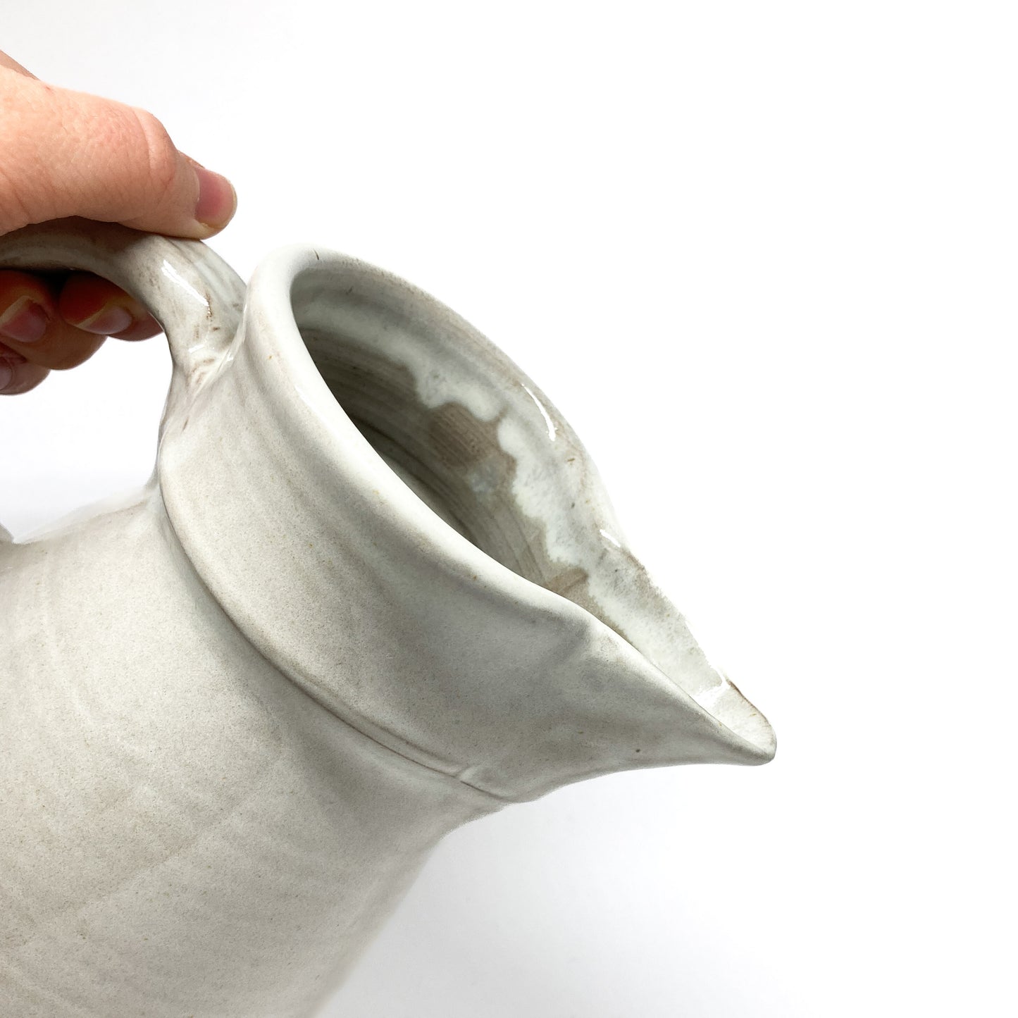 Hand holding a speckled, glazed ceramic pitcher by its curved handle, showing the flared spout.