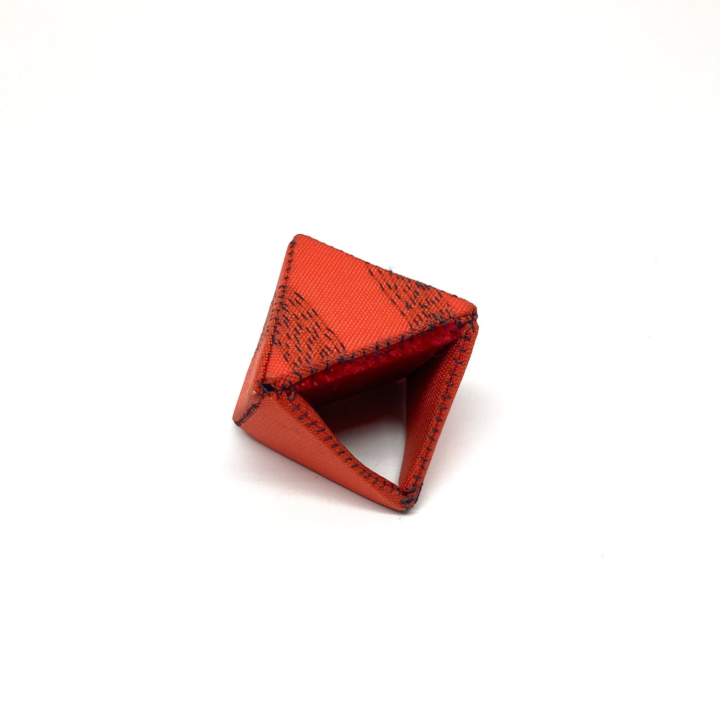 An orange Flagged Ring, a triangular form with dark stitching, rests on a light surface.