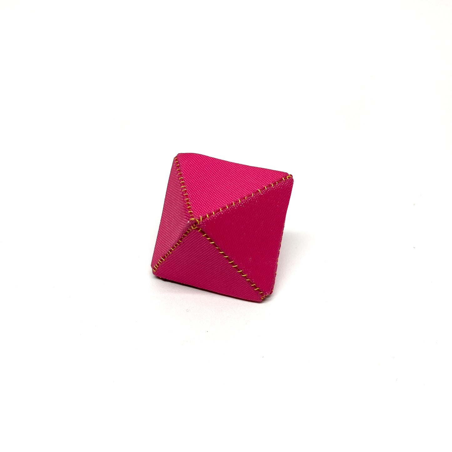 A pink Flagged Ring, a geometric shape with light-colored stitching, sits on a surface.