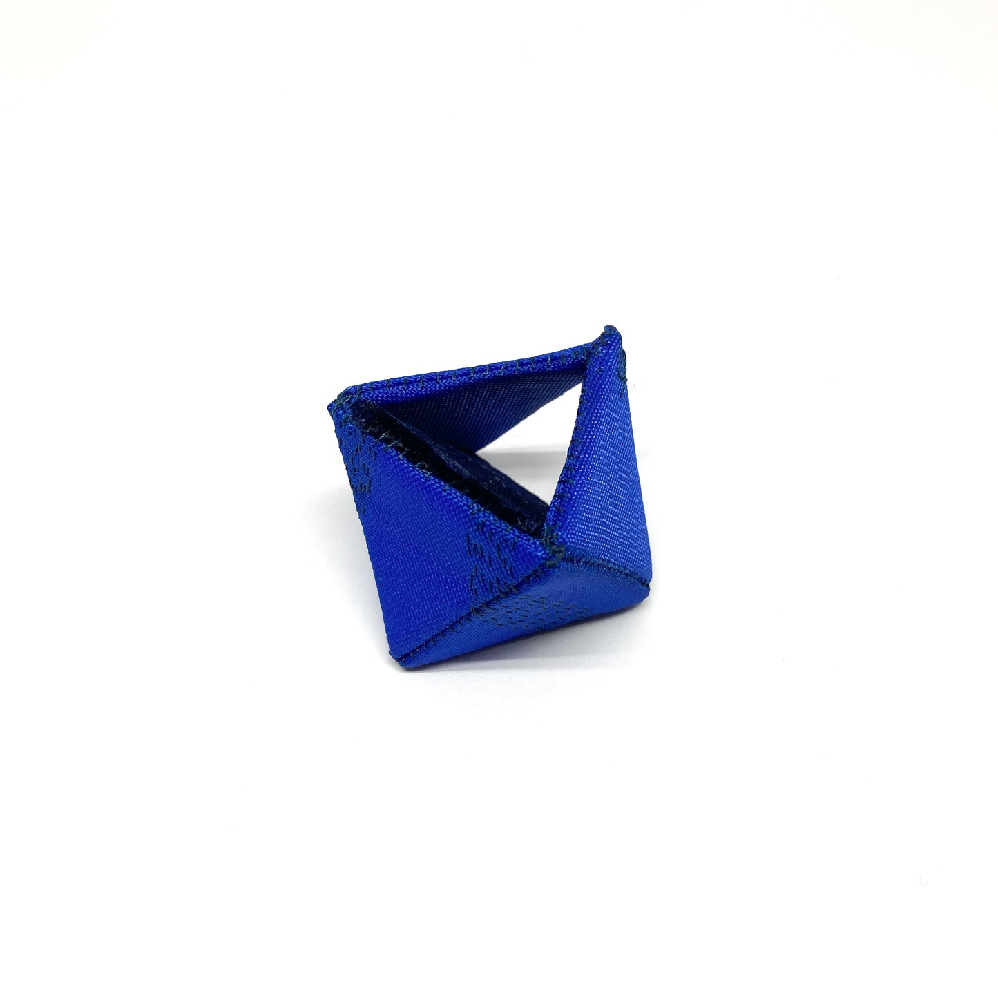 A blue Flagged Ring, a geometric form with dark stitching, rests on a surface.