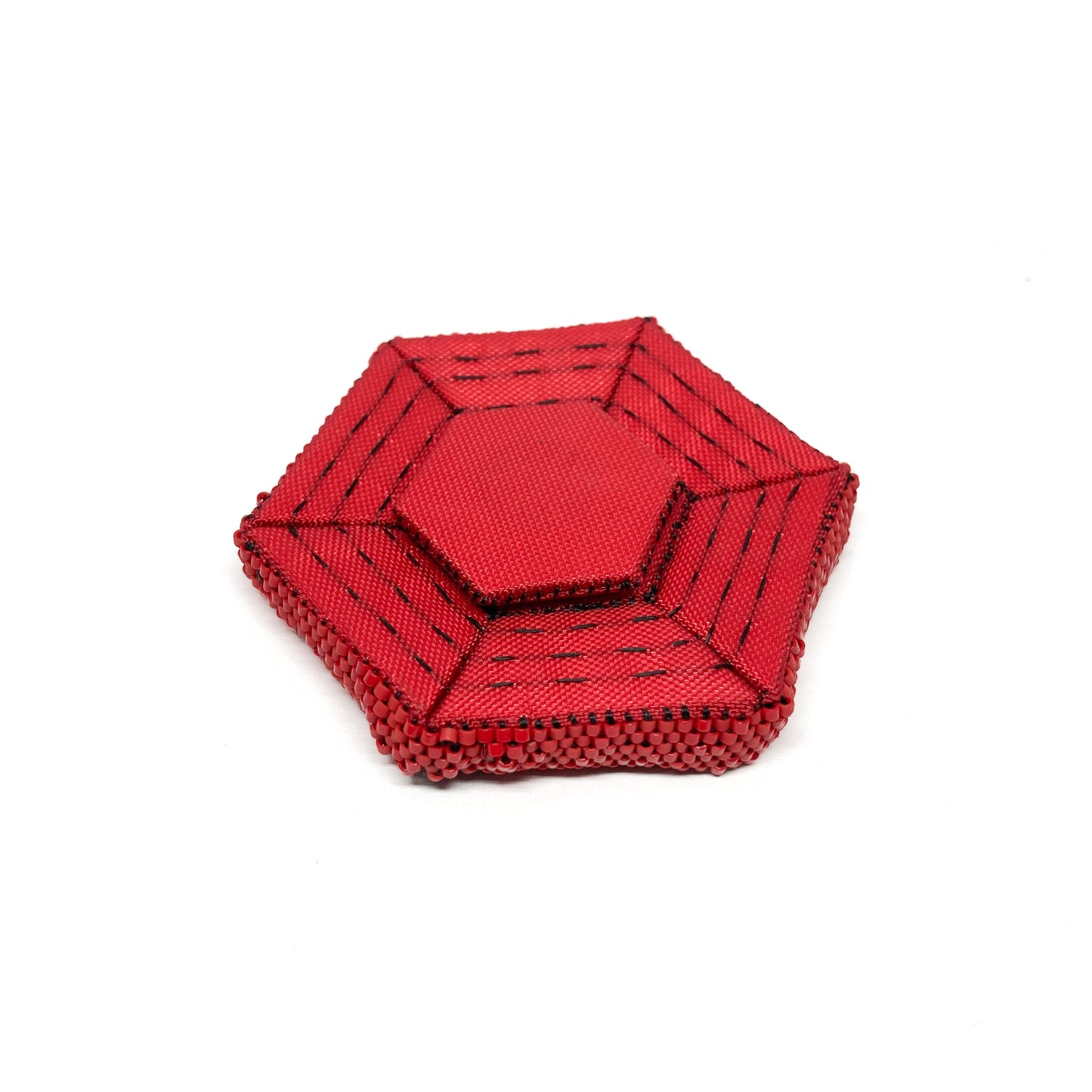 Overhead view of a red, beaded Flagged Obsessions Brooch featuring black accents and a hexagonal shape.