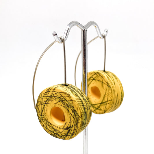 Two yellow and green striped donut-shaped earrings hang from a silver display stand.