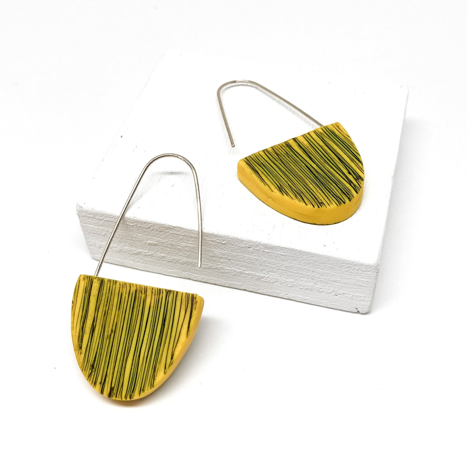 Two yellow, half-circle earrings with black scribbled lines hang from silver hooks.