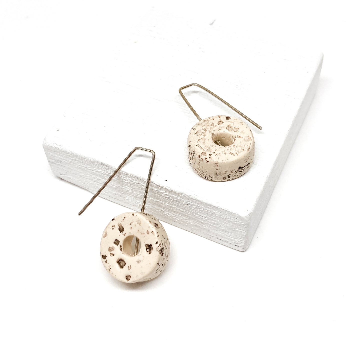 Two white, donut-shaped earrings with brown speckles hang from silver hooks.