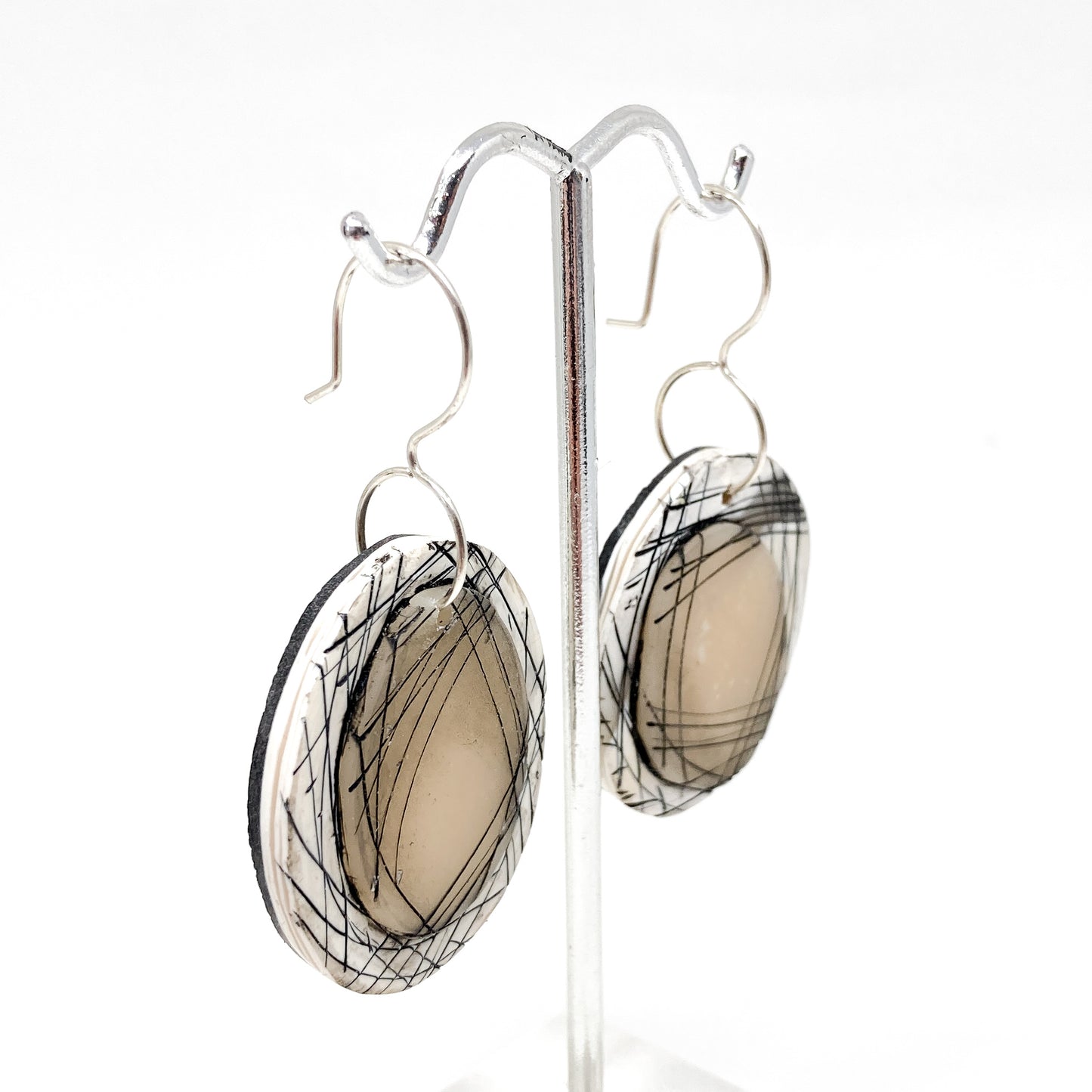Side view of round dangle earrings with abstract black line design on a layered circular base, hanging on a metal stand.
