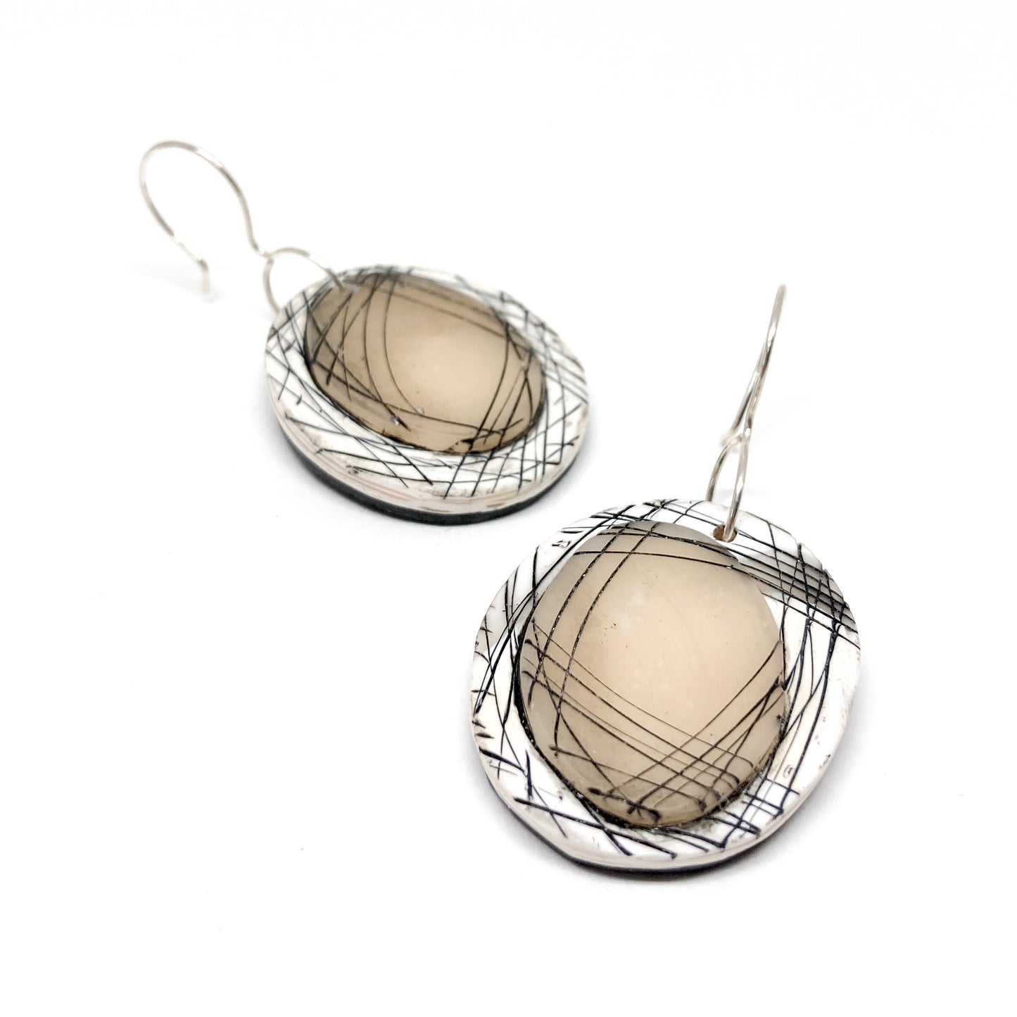 Pair of round artisan earrings with abstract black linework, displayed lying flat with visible metal hooks.