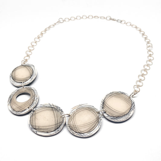 Statement necklace with five round abstract pendants featuring black line designs, linked by a circular chain.