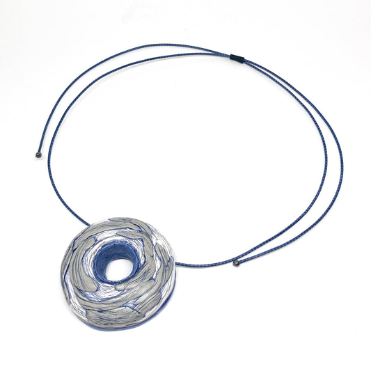 Textured circular pendant with central opening on a cord necklace, shown from a top view.