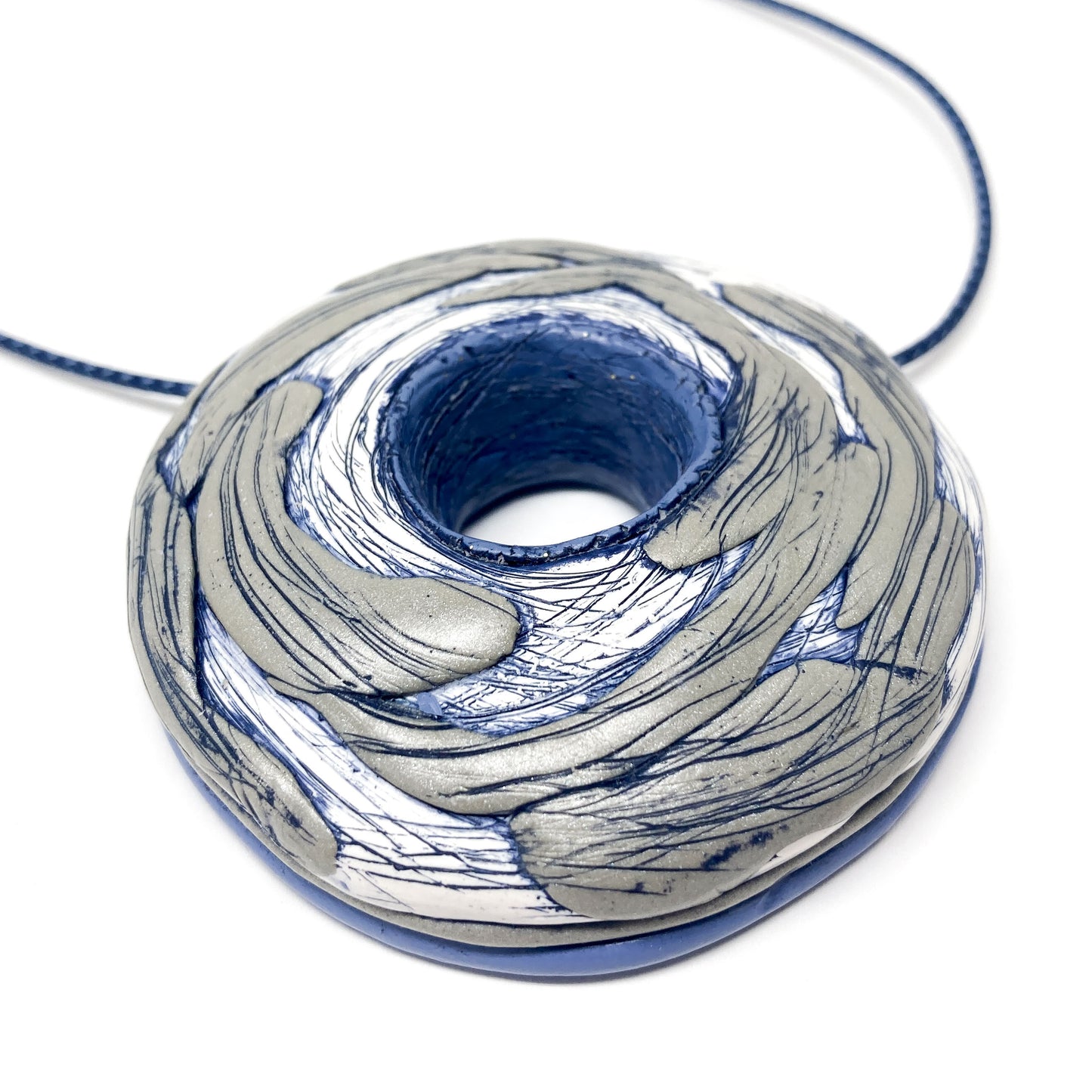 Close-up of a sculptural round pendant with swirling textured surface and central hole on a cord necklace.