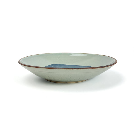 Shallow, light-colored ceramic bowl with a dark rim and a bold blue rectangular design on the interior.
