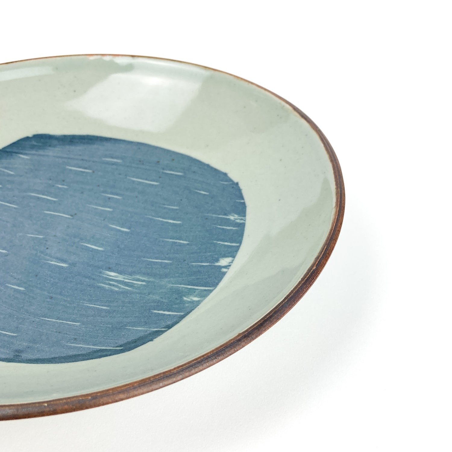 Close-up of a light ceramic bowl with a dark rim and a blue, slightly irregular circular design with white lines inside.