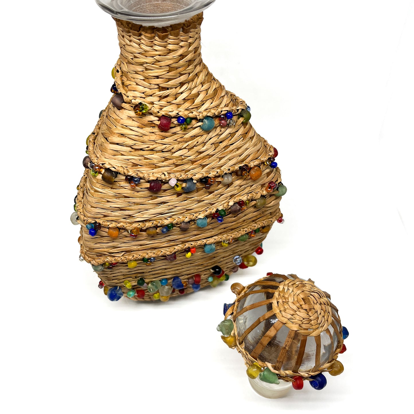 A decanter and its stopper, both wrapped in woven material and adorned with colorful beads.