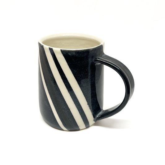 A ceramic mug with bold, diagonal black and white stripes and a black handle. The inside of the mug is a light color.