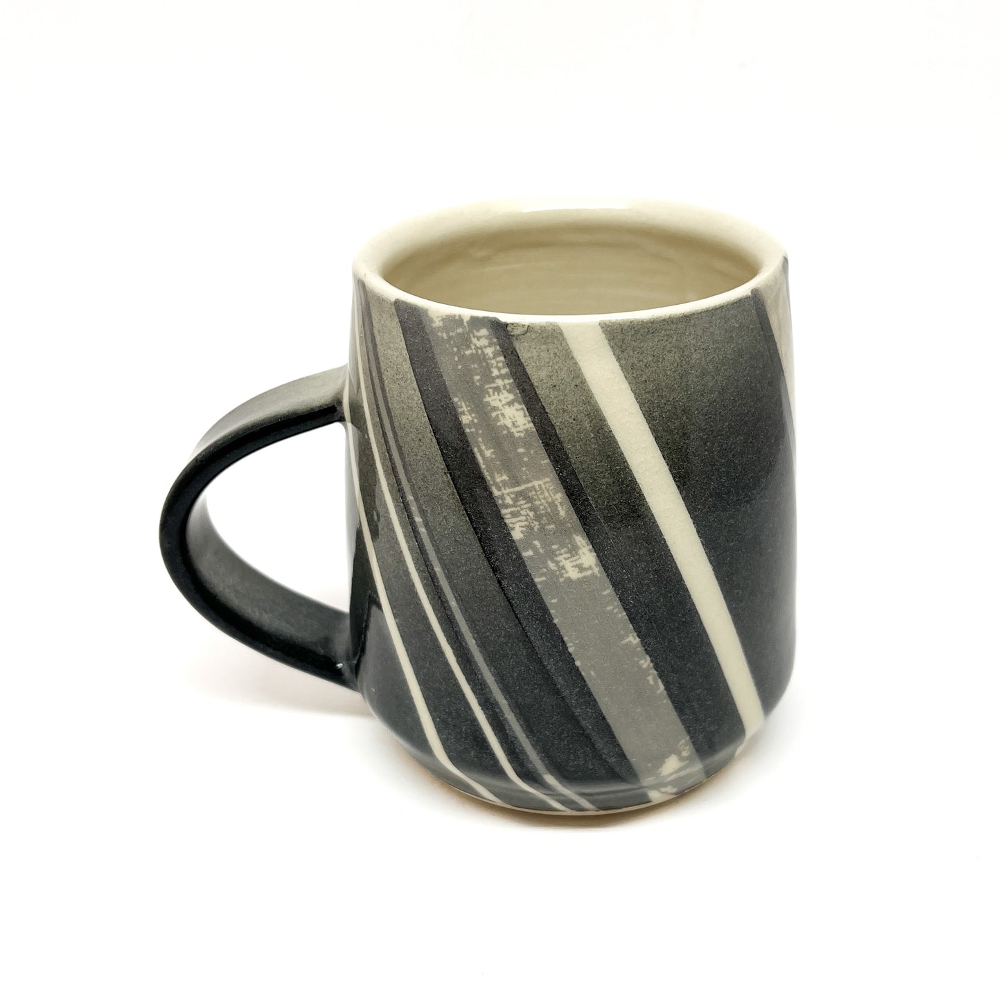 A ceramic mug, possibly wood-fired, with diagonal stripes in shades of gray and white, and a dark handle. The inside is a light tone.
