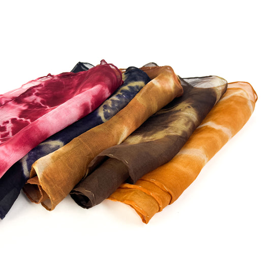 A collection of six uniquely patterned and colored silk scarves are loosely piled, showcasing their individual textures and designs.