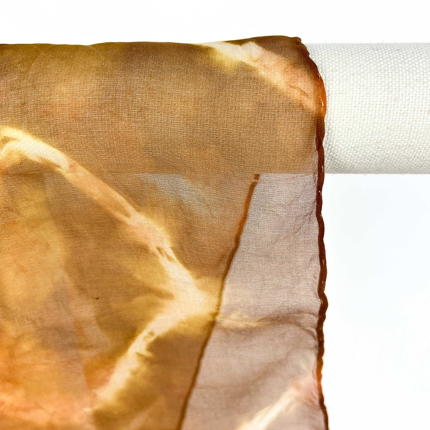 A close-up shows the delicate weave and circular resist shibori pattern of a Tea silk scarf draped over a white bar.