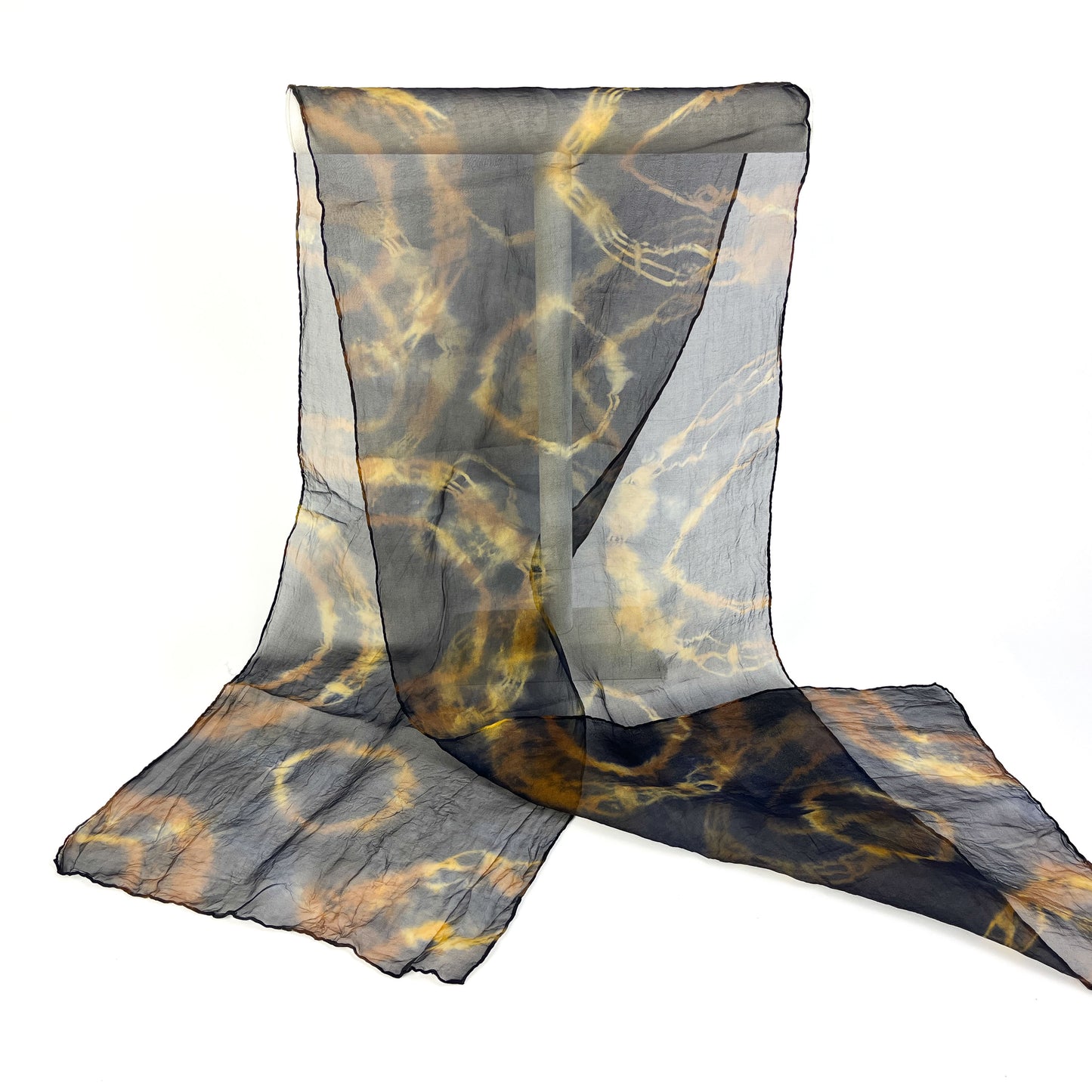 A sheer silk scarf with a dynamic, swirling resist shibori pattern is partially draped over a white surface.