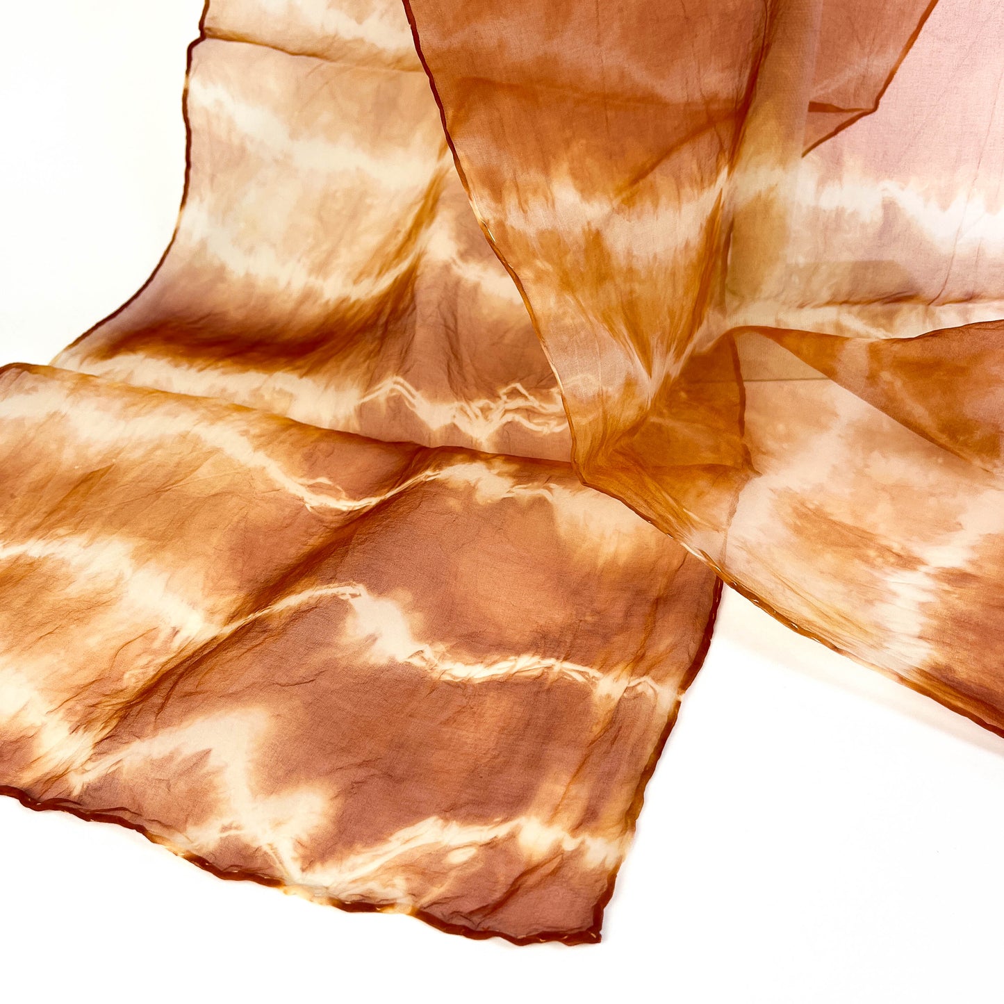 A close-up shows the delicate weave and horizontal tie-dye pattern with subtle texture on a sheer silk scarf.