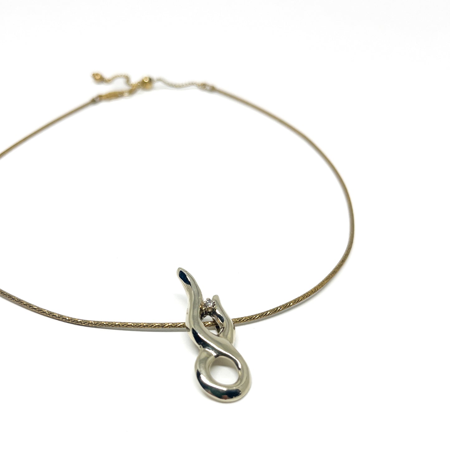 A delicate gold necklace featuring a polished silver abstract pendant with a small, sparkling stone.