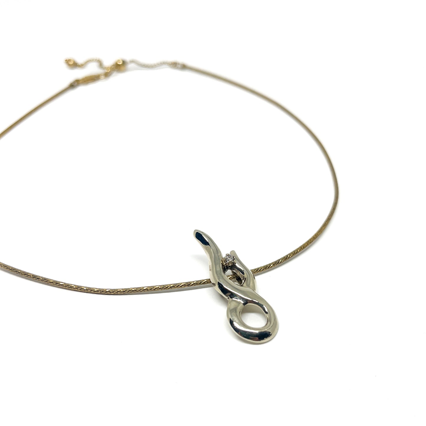 A fine gold necklace featuring a sleek, polished silver abstract pendant with a small, brilliant gemstone.