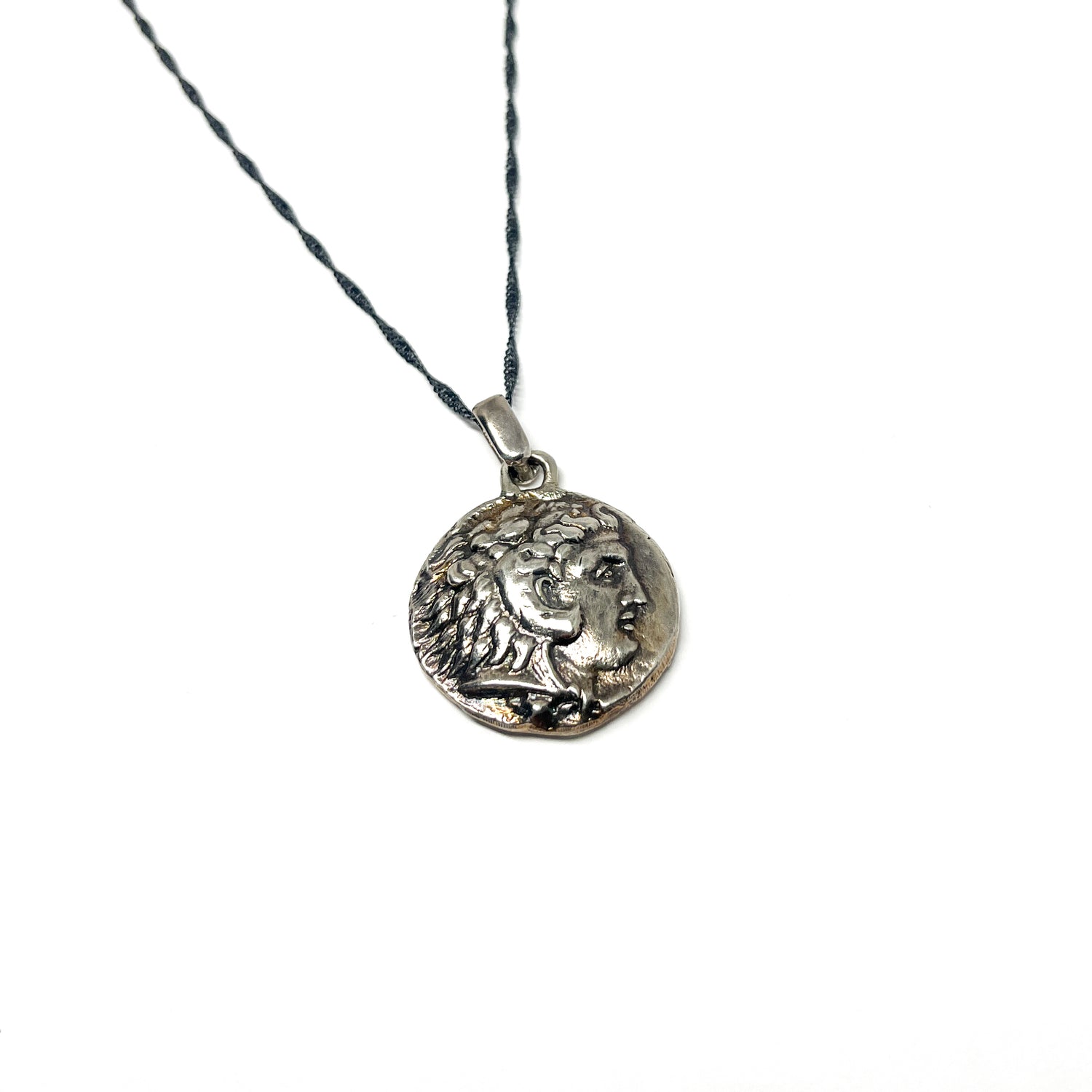 Close-up of a silver necklace with a dark chain and a round pendant featuring a detailed profile, possibly Ancient Roman art.