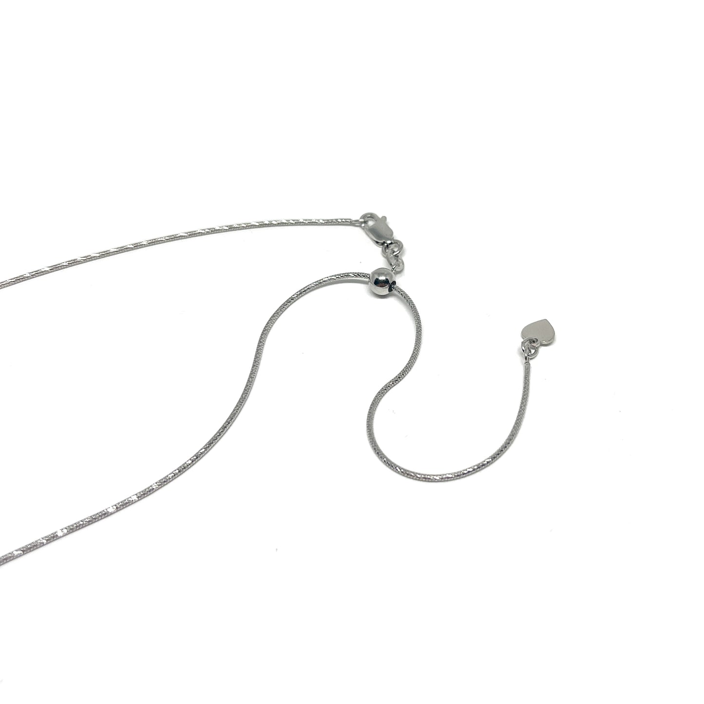 Close-up of a delicate silver necklace with an adjustable diamond-cut snake chain and a small heart charm at the end.