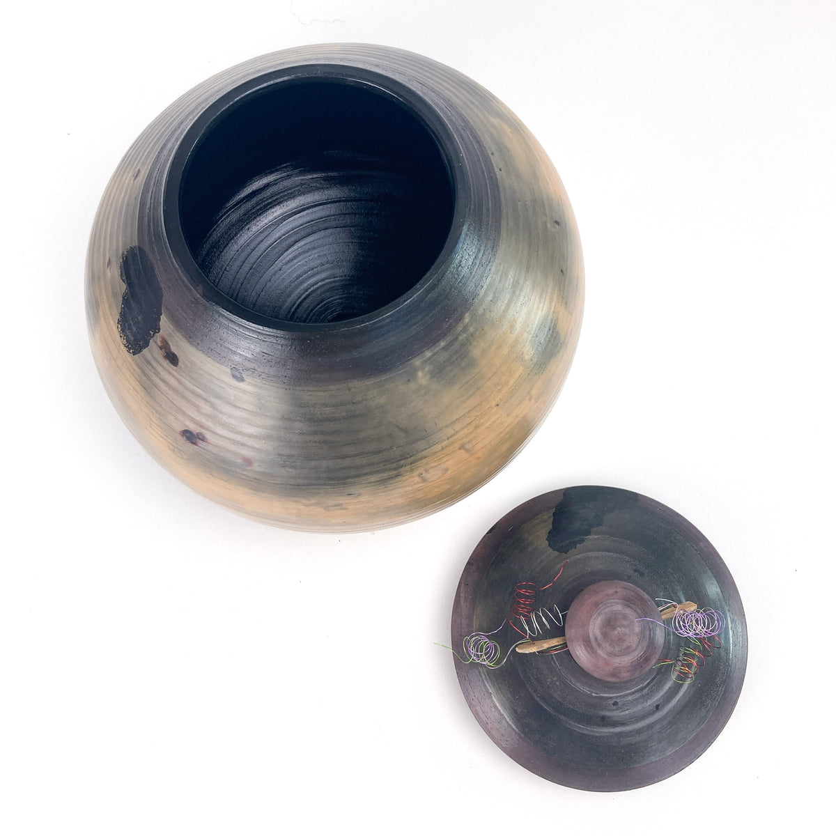 Open handmade ceramic pot with textured interior, lid with knob and twine detail beside it.