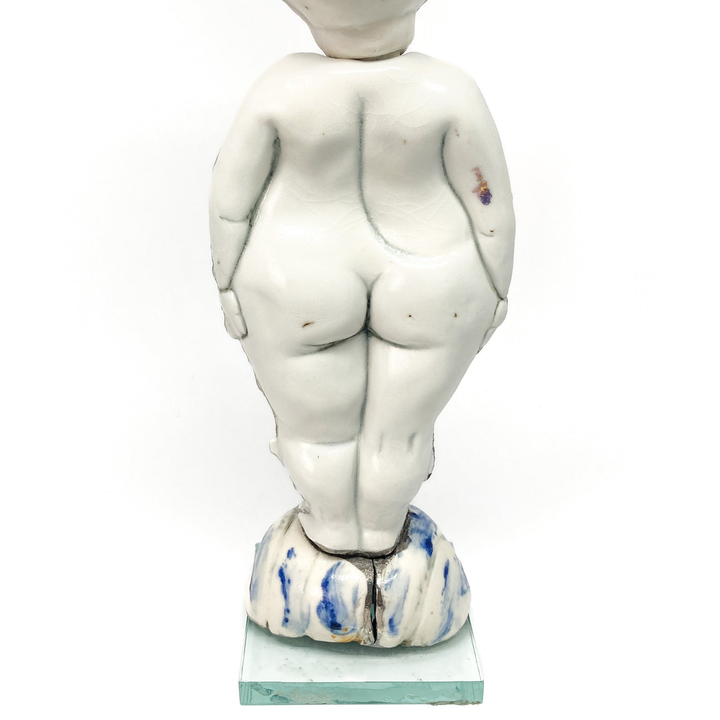 The back of a white ceramic figurine of a child stands on a decorated base with blue and white elements.