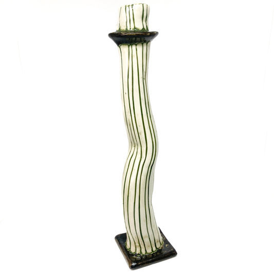 A white ceramic candlestick with wavy form features dark green vertical stripes. The base and top rim are also dark green.