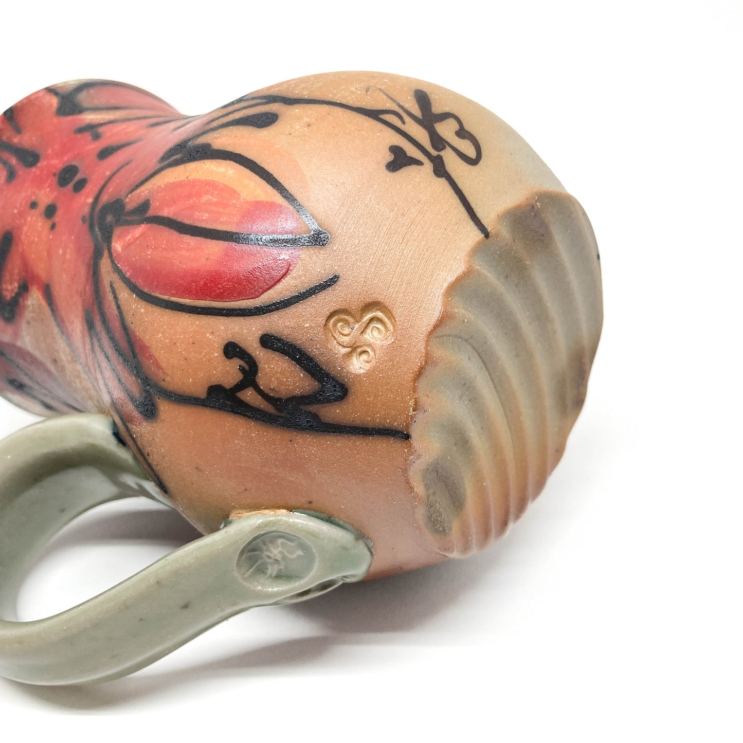 A ceramic mug with a handle, viewed from the side, showing a hand-painted floral design and a maker's mark. The mug has a smooth, glazed finish.