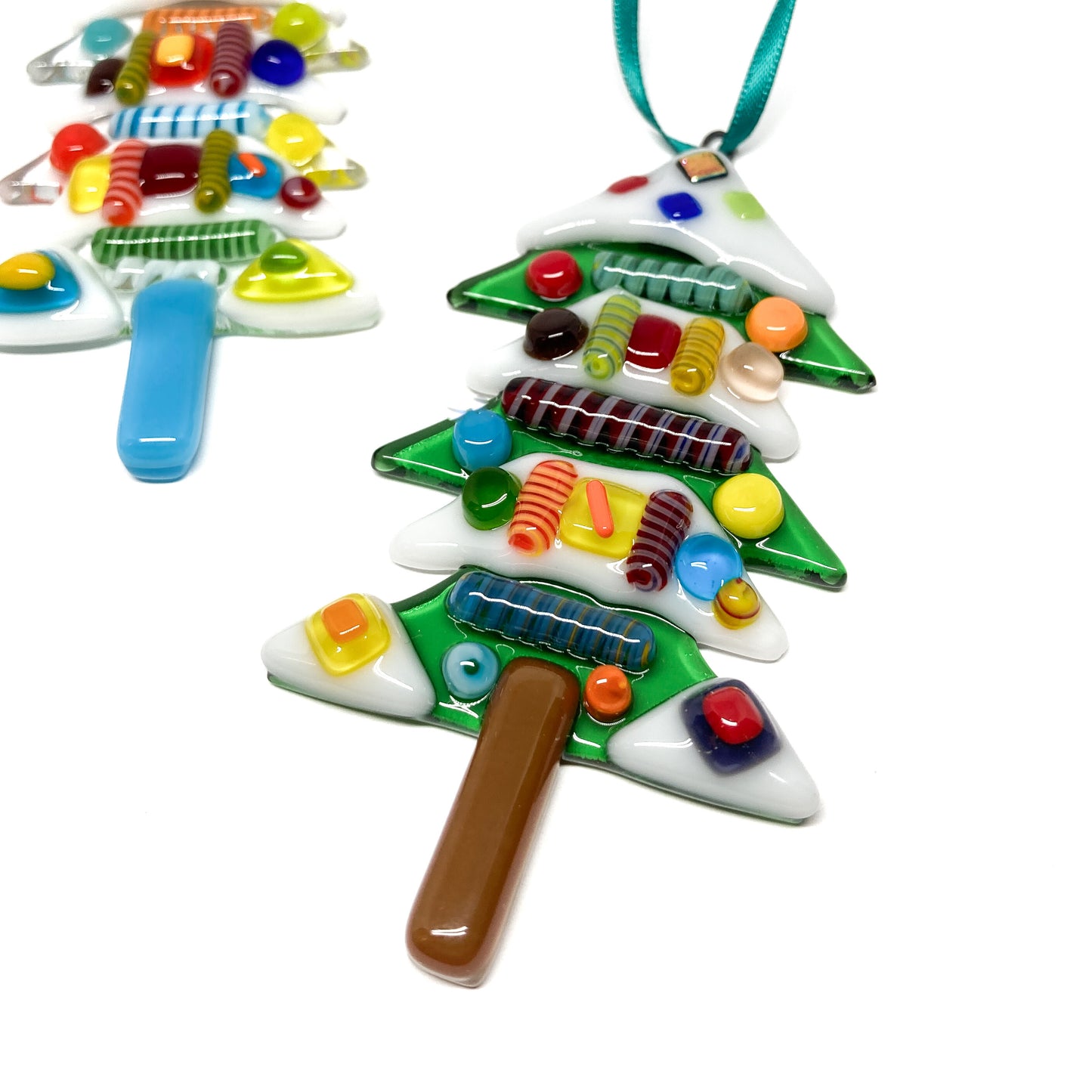 Two fused glass Christmas tree ornaments decorated with colorful glass pieces, one with a ribbon for hanging.