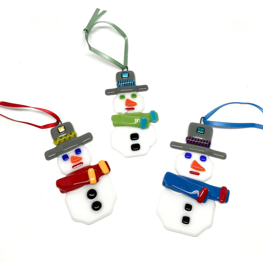 Three fused glass snowman ornaments with colorful scarves and hats, each with a ribbon for hanging.
