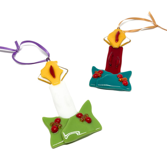 Two glass candle ornaments with colorful details and ribbons, viewed from above.