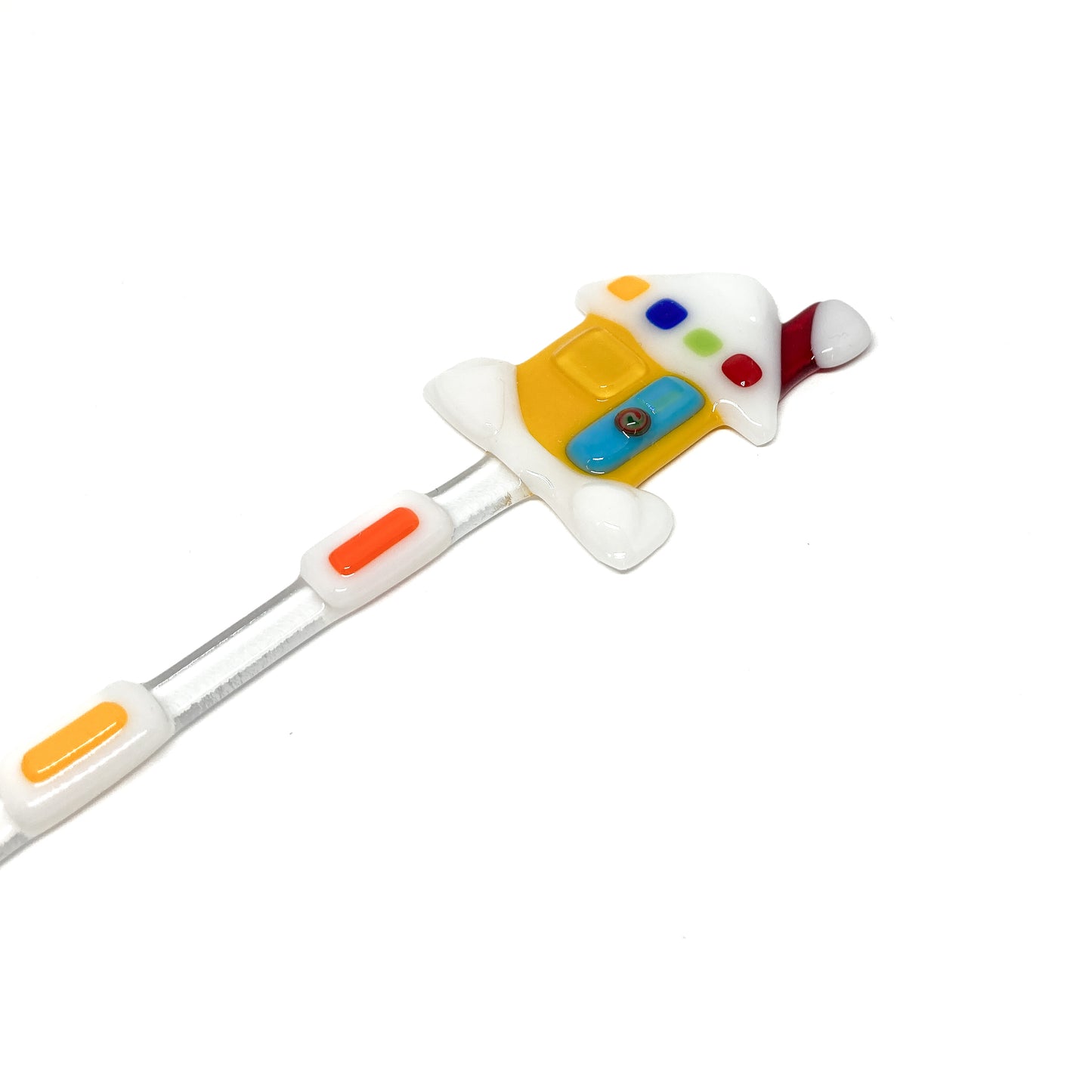 A glass stir stick shaped like a house, decorated with colorful glass pieces.