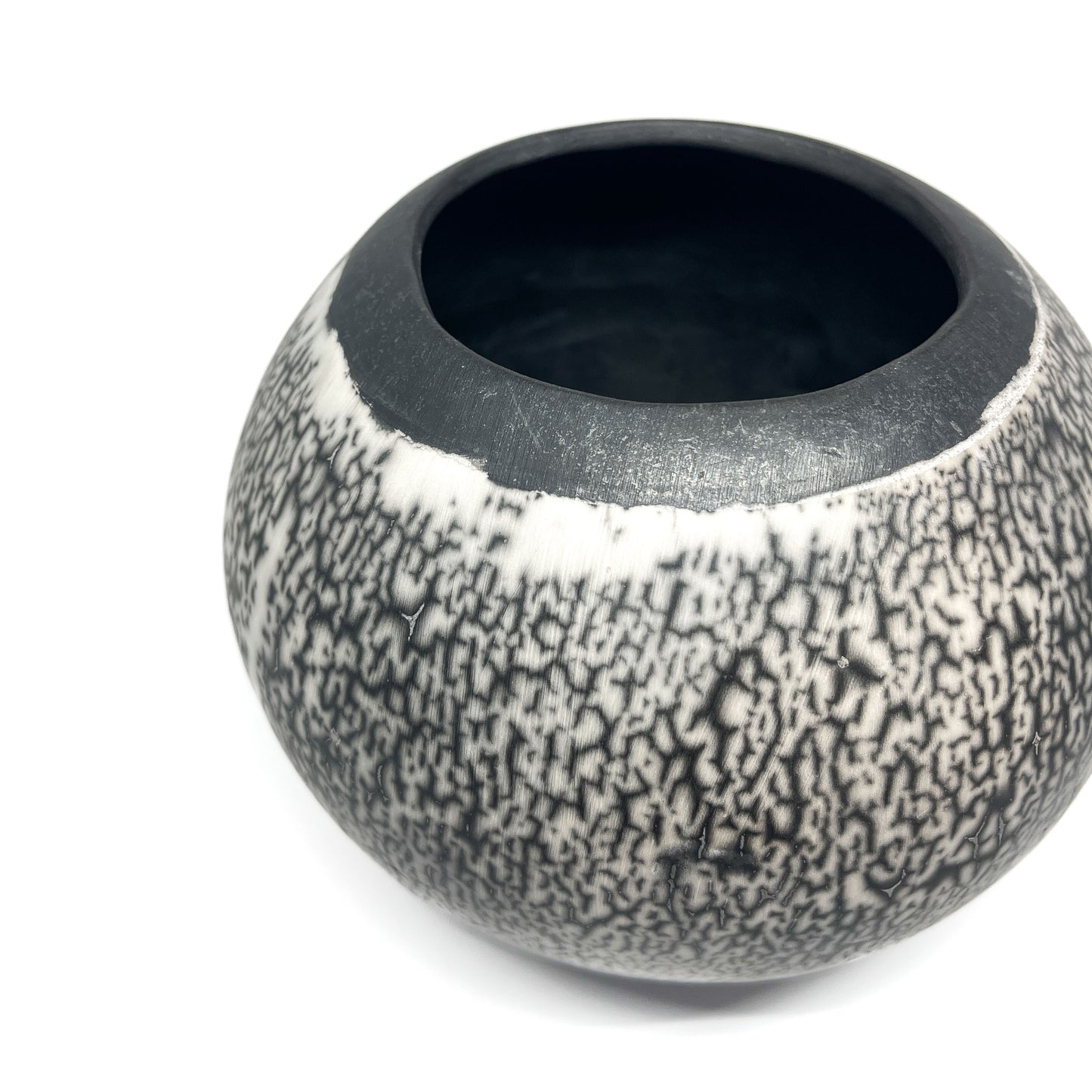 Angled close-up of a round ceramic vase with a textured, crackled black and white exterior and black interior.