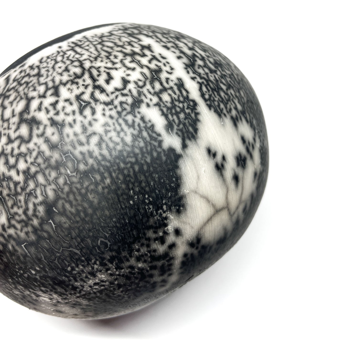 Close-up of a round ceramic object with a textured, crackled black and white glaze.