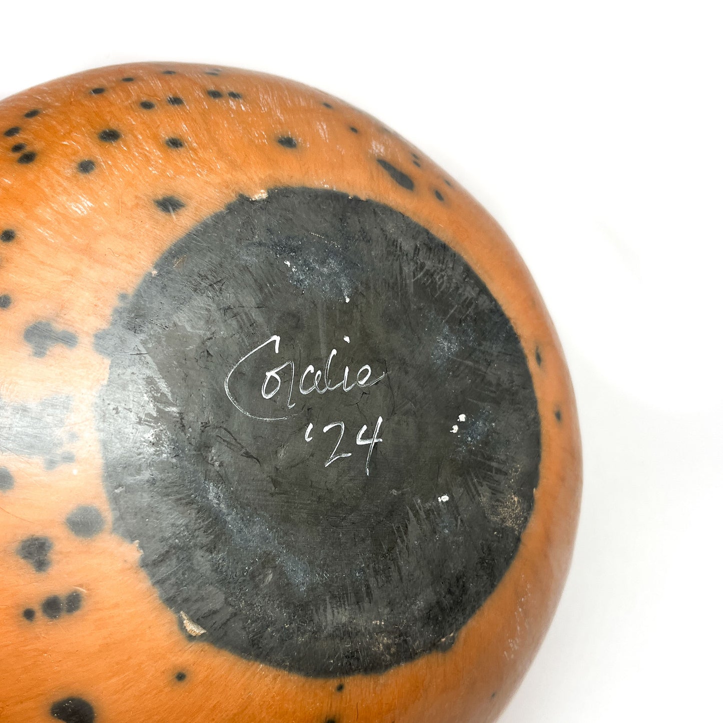 Close-up of the top of a round ceramic vase with a mottled glaze and handwritten text within a dark circle.